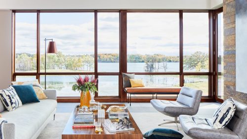 Spacious living room with large windows showcasing a serene lakeside view and cozy seating.
