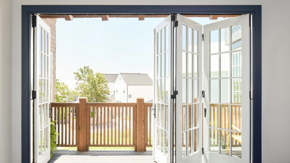 Open bi-fold doors lead to a sunlit balcony overlooking a welcoming neighborhood.