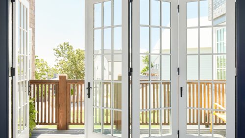 Bright bifold doors open to a sunny deck with a warm, welcoming neighborhood view.