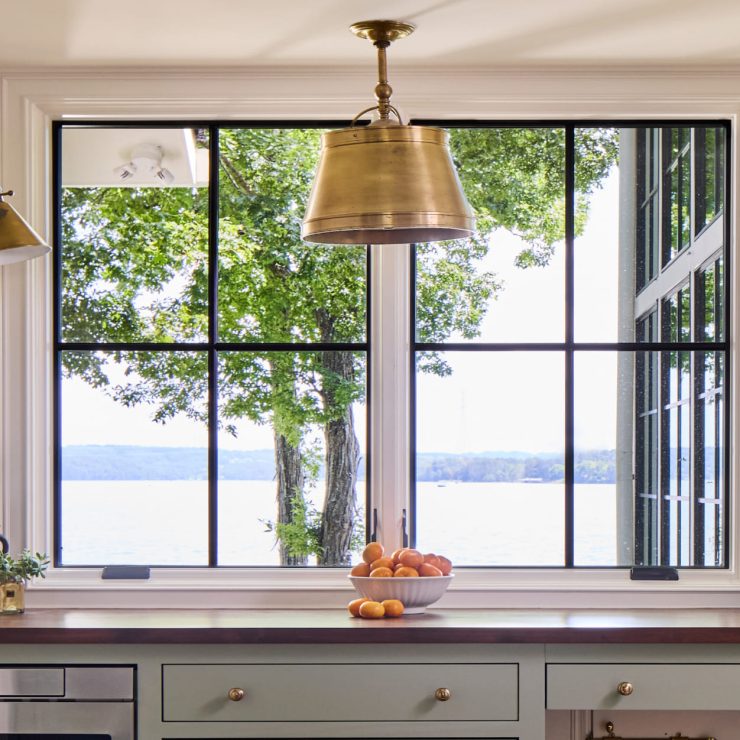 Bright kitchen with black casement window overlooking a peaceful lake and trees.