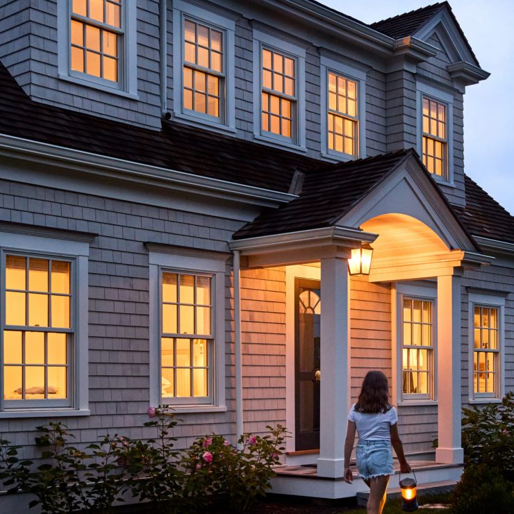 Warmly lit home with classic double-hung windows welcoming a visitor in the evening.