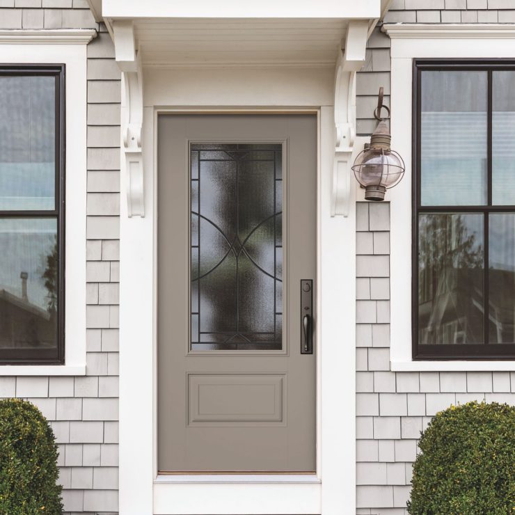 Welcoming front door with frosted glass and classic trim framed by two windows and greenery.