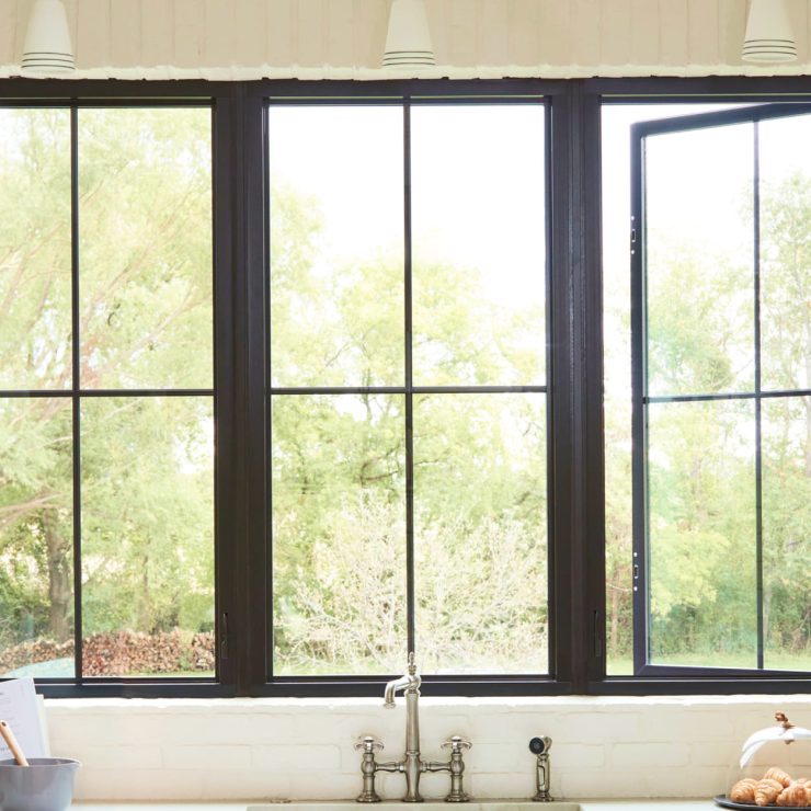 Bright kitchen with black-framed fiberglass windows opening to lush green outdoors.