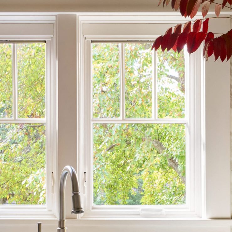Bright kitchen windows framed by wood offer a clear view of lush green trees, inviting natural light.