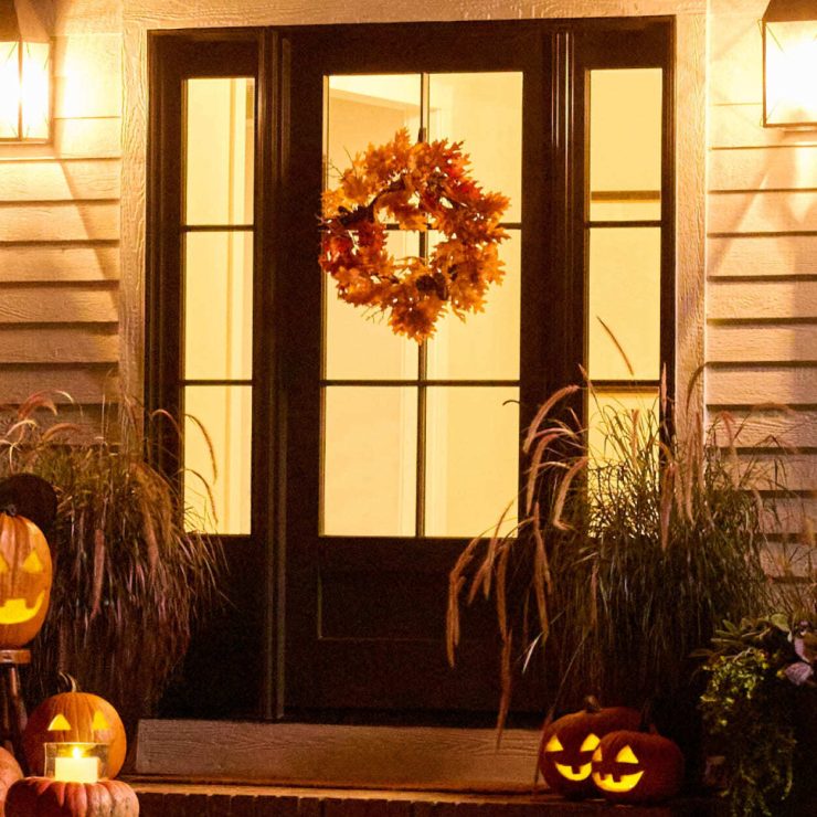 Warmly lit front door with autumn wreath and festive carved pumpkins welcoming guests.